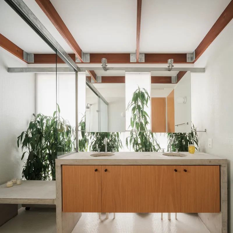 Bathroom vanity with timber cabinetry and concrete surround, exposed beams above, potted plants reflecting in mirror