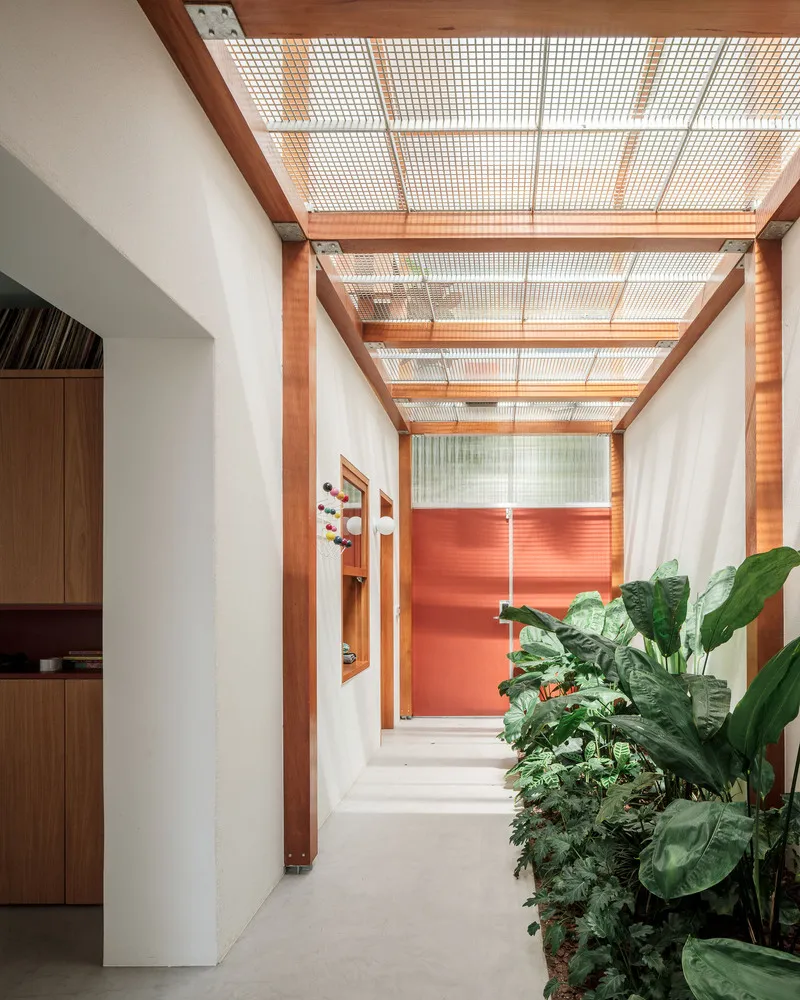 Interior view through timber framed pergola to red tile wall and planted courtyard in bright daylight
