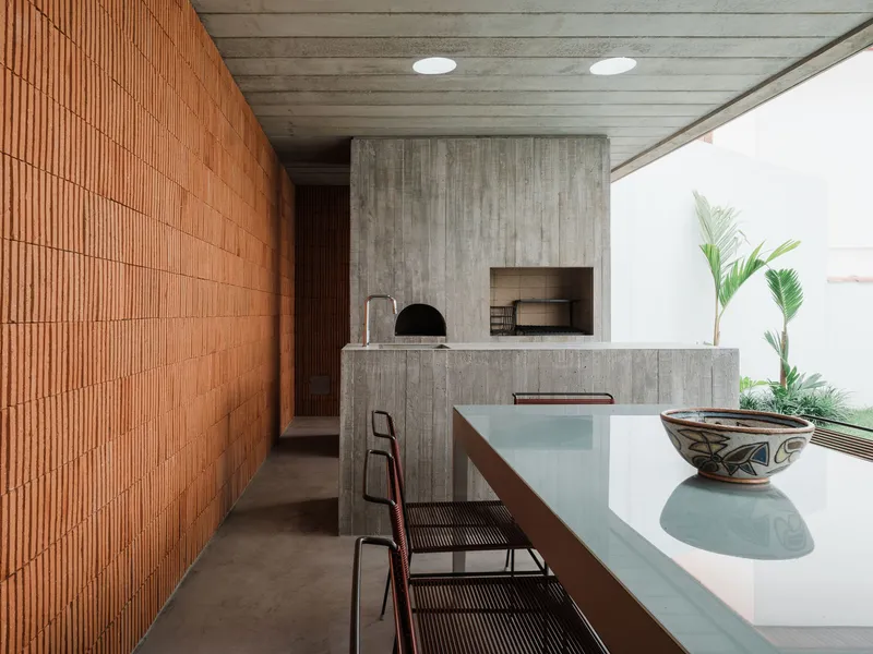 Covered outdoor kitchen with board-formed concrete island, pizza oven, red tile wall and concrete plank ceiling