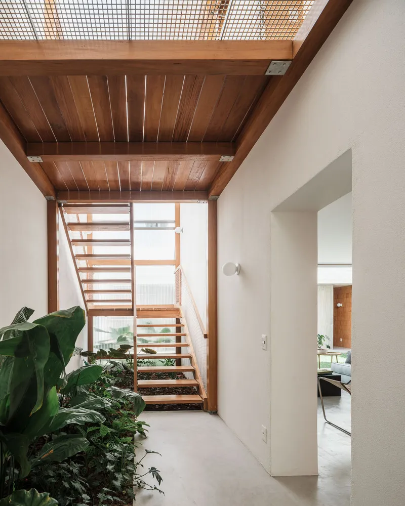 Open timber staircase with exposed beams and planted beds along white walls below a translucent ceiling panel