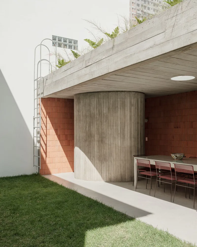 Outdoor terrace with cylindrical concrete column, board-formed soffit, red brick wall and metal ladder to roof garden