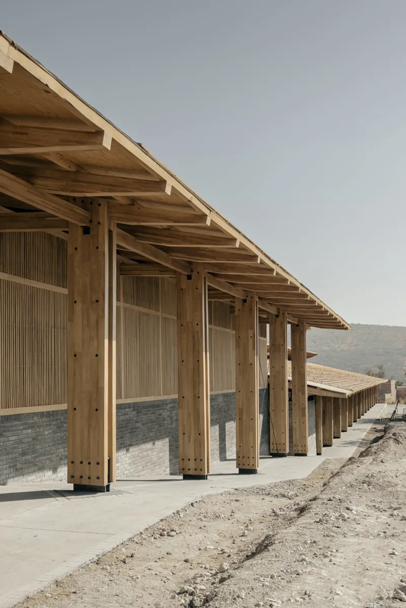 Covered walkway with exposed timber columns and beams under a shallow-pitched roof in afternoon sun