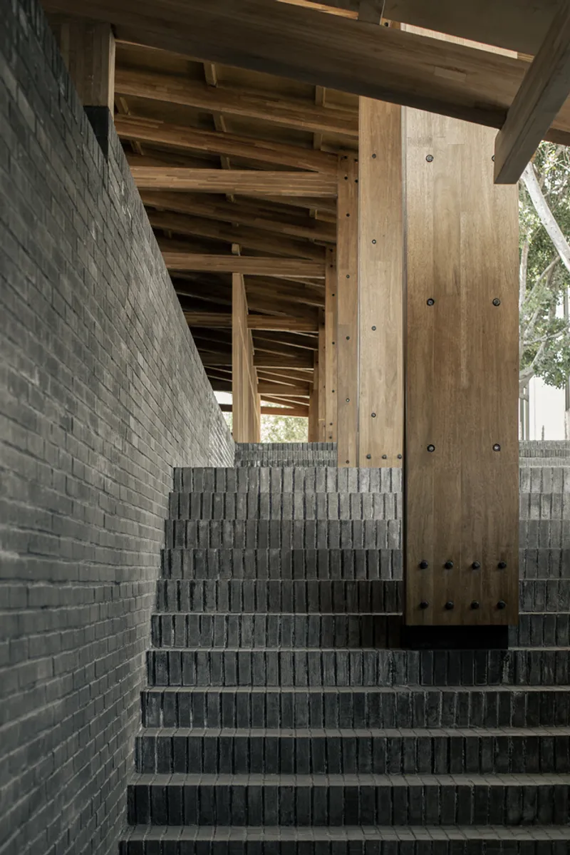 Grey brick staircase with timber columns and exposed rafters visible beneath the wooden ceiling above