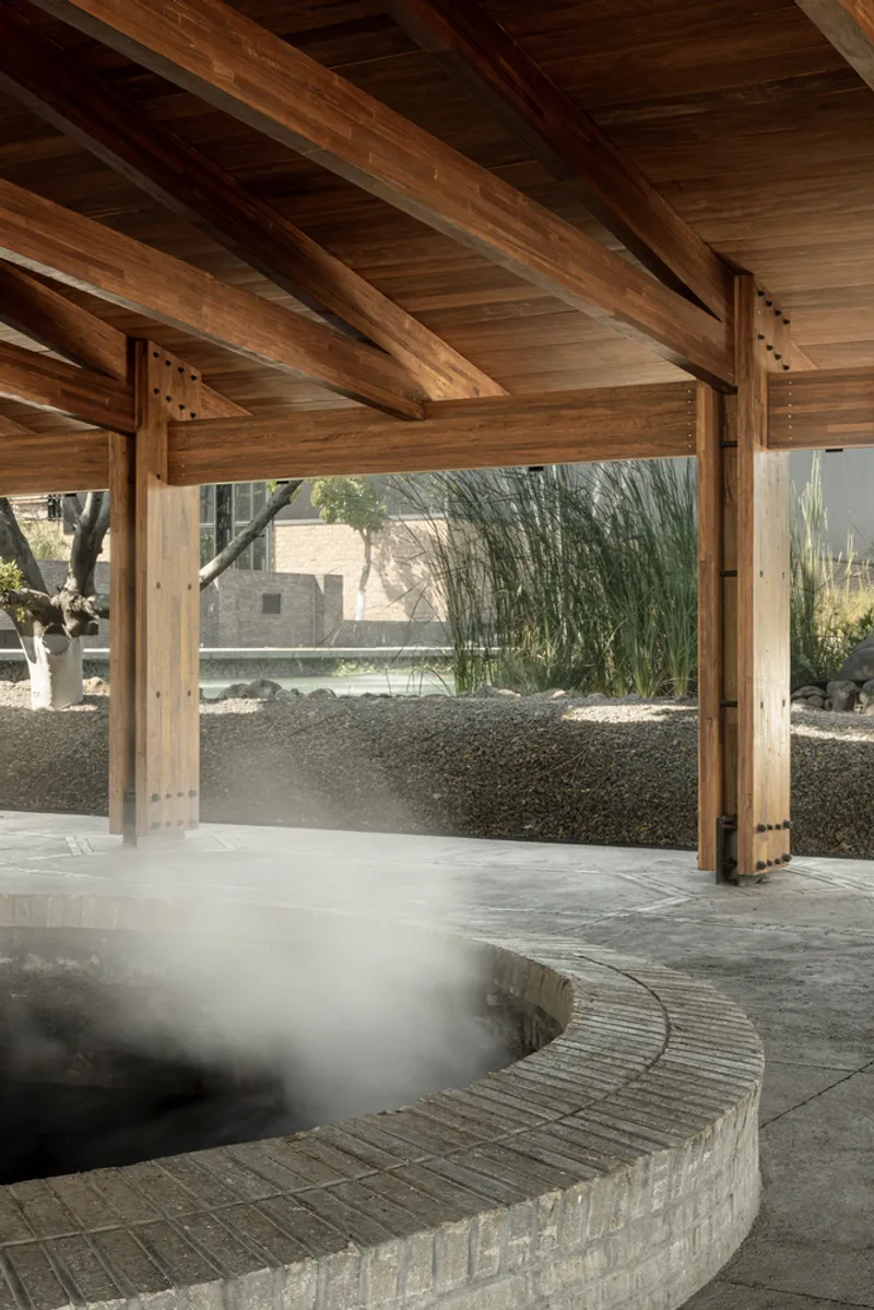Circular brick-clad water feature with steam rising under a timber post and beam pavilion