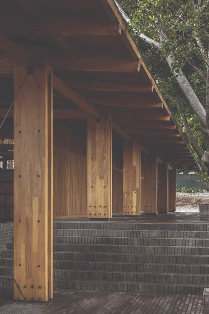 Timber columns and grey brick low wall under a cantilevered roof with trees visible beyond