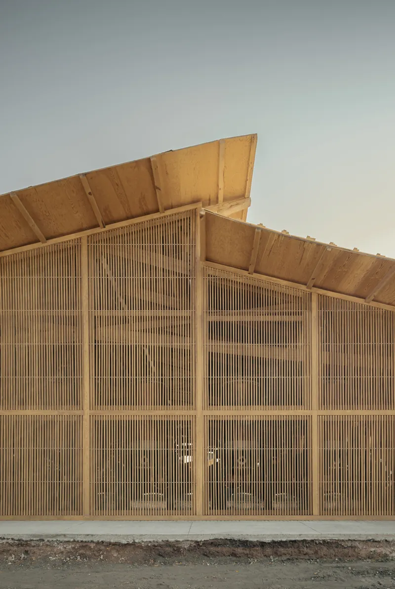 Vertical timber louvered facade rising to a sloped roof under evening light