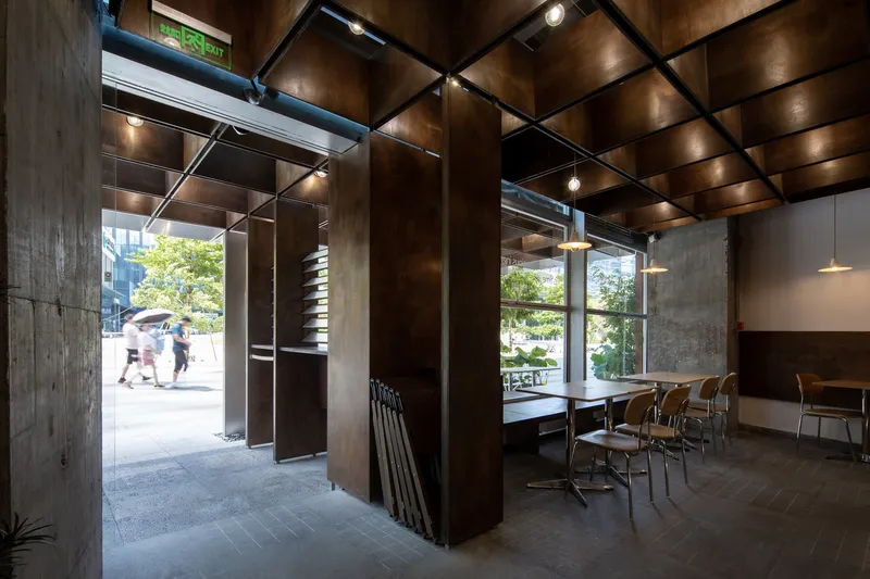 Interior dining area with coffered timber ceiling, steel columns, and glazed storefront opening to pedestrians outside