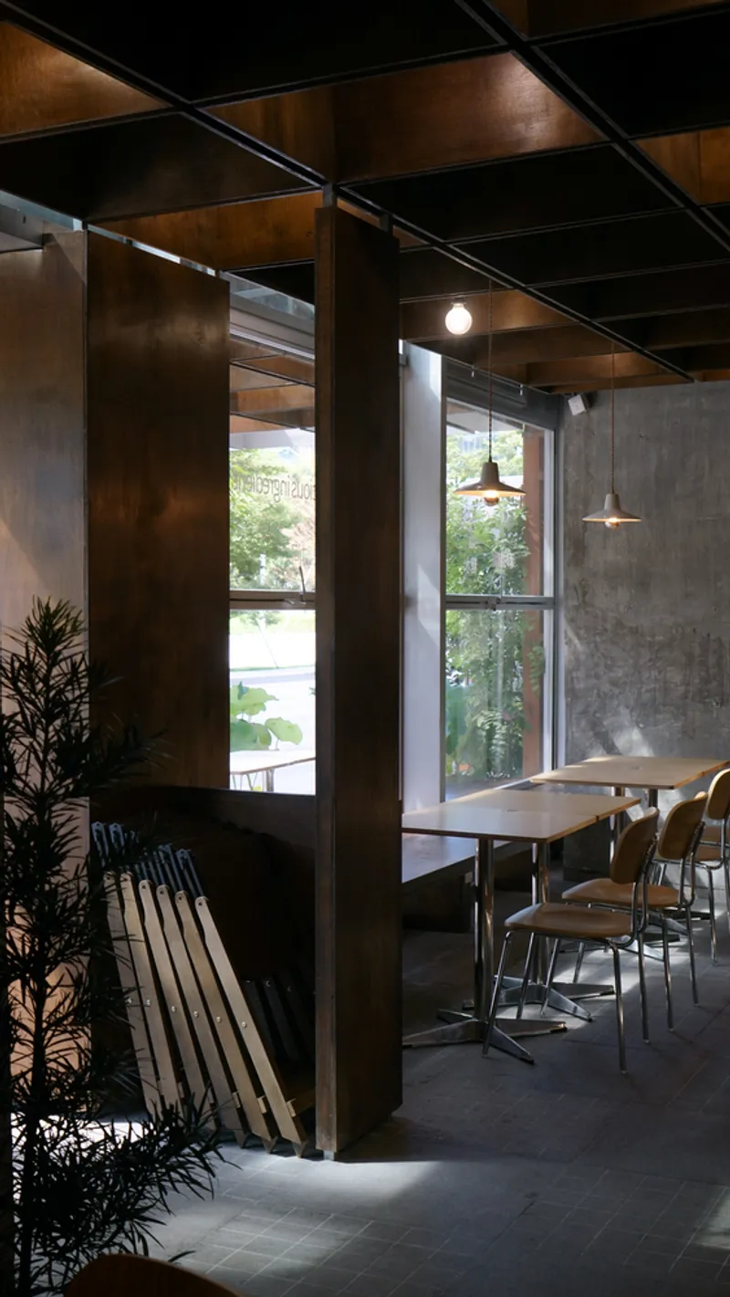 Corner seating nook with dark timber columns, potted plant, and pendant lights beside street-facing windows