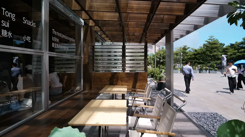 Covered outdoor seating area with timber ceiling and steel columns adjacent to a glass storefront and plaza