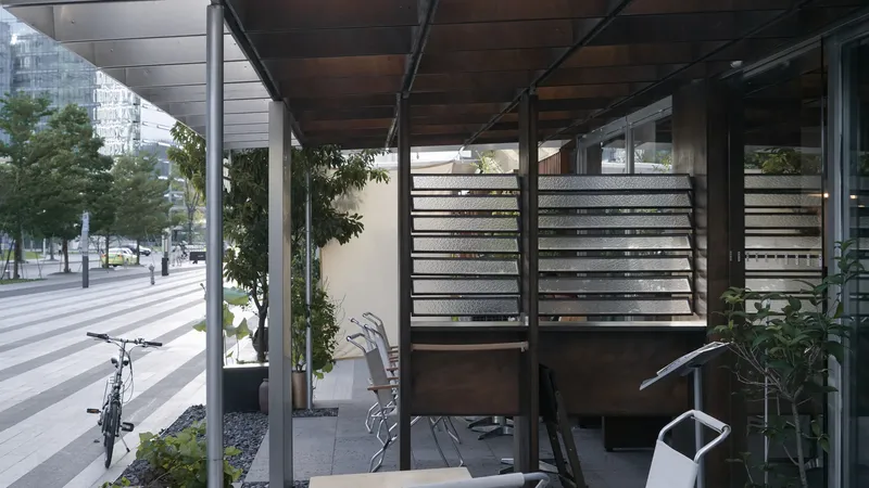 View through the open pavilion showing horizontal slatted screens and steel structural frame with pedestrians beyond
