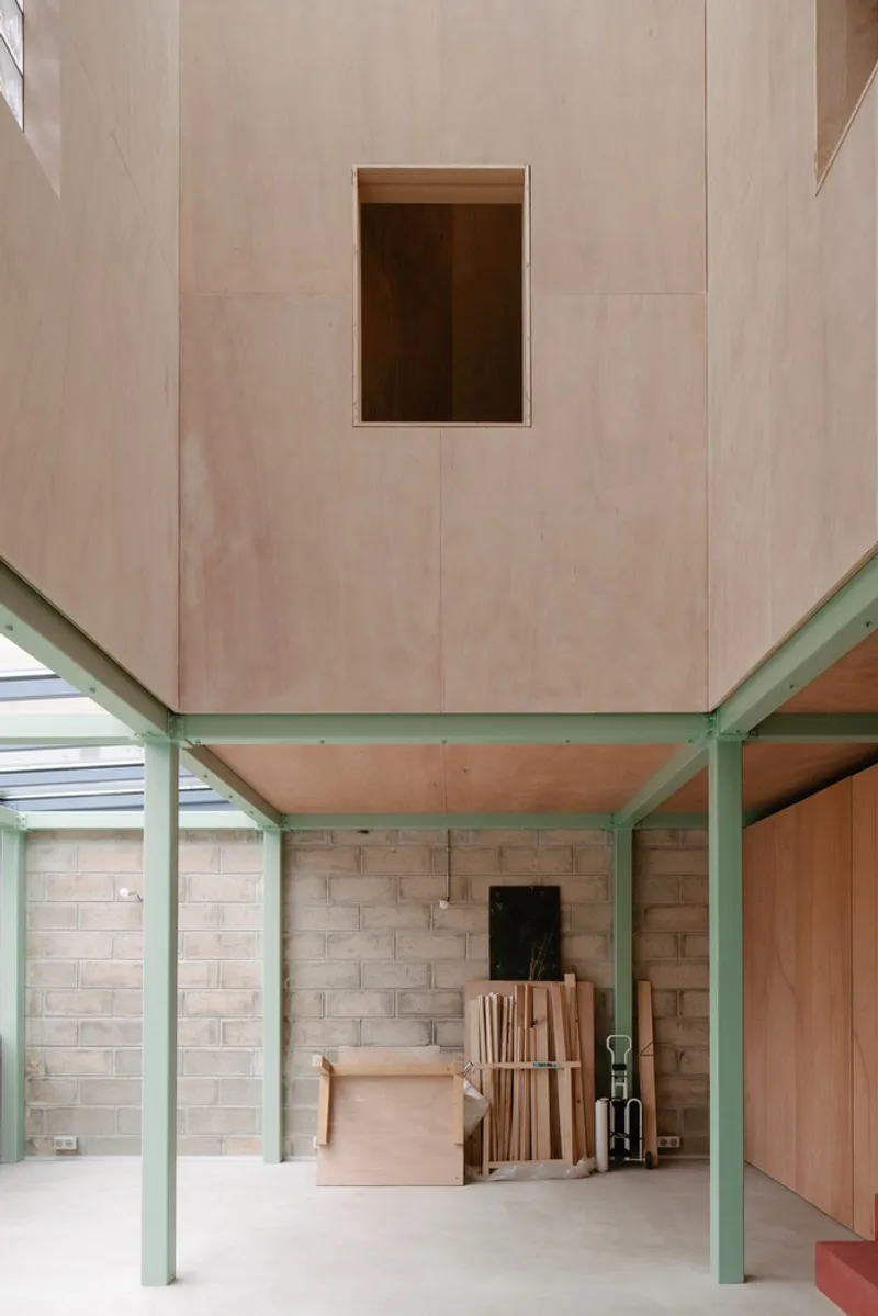 Ground floor space with pale plywood ceiling above green steel columns and concrete block walls