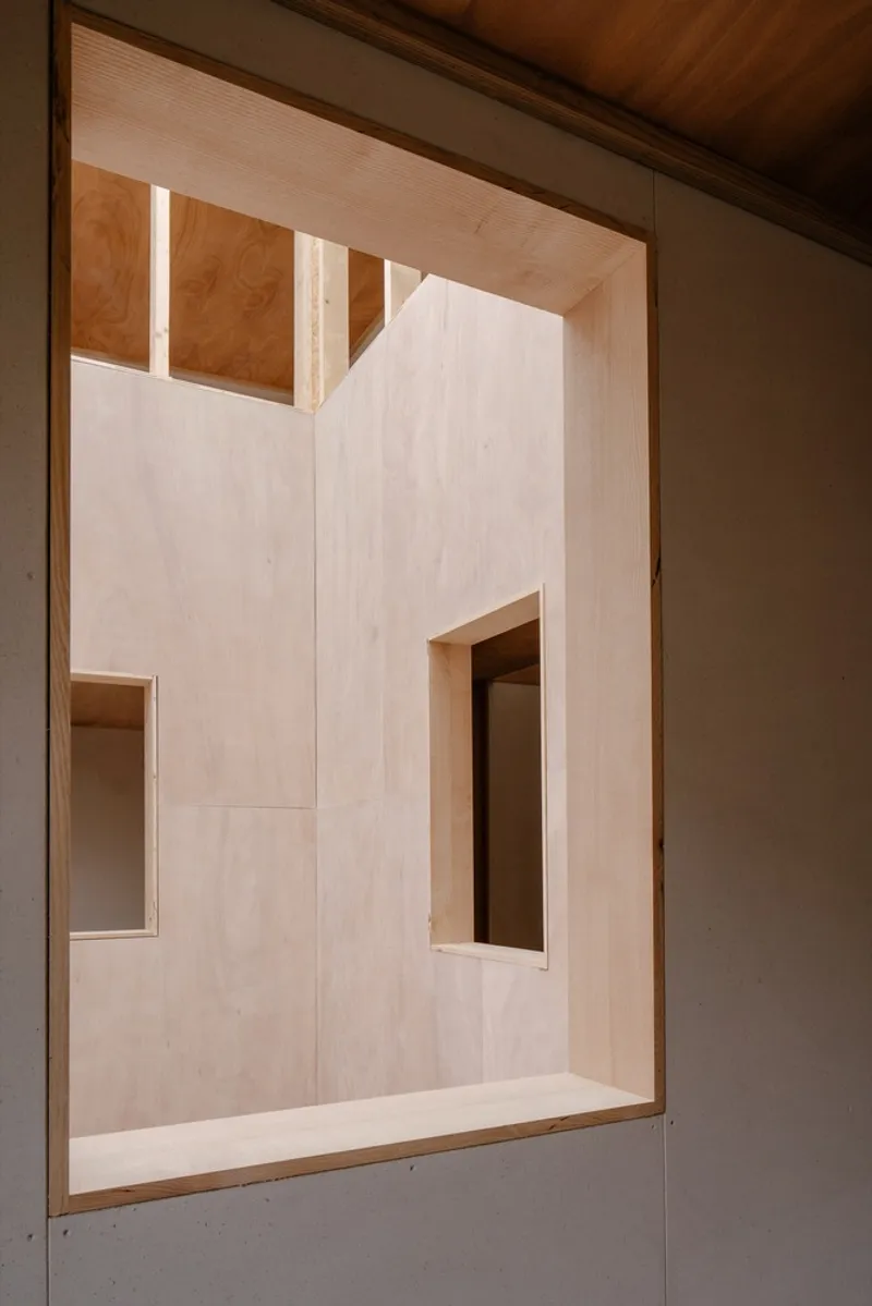 View into a plywood-lined room with clerestory windows and integrated shelving under a timber ceiling