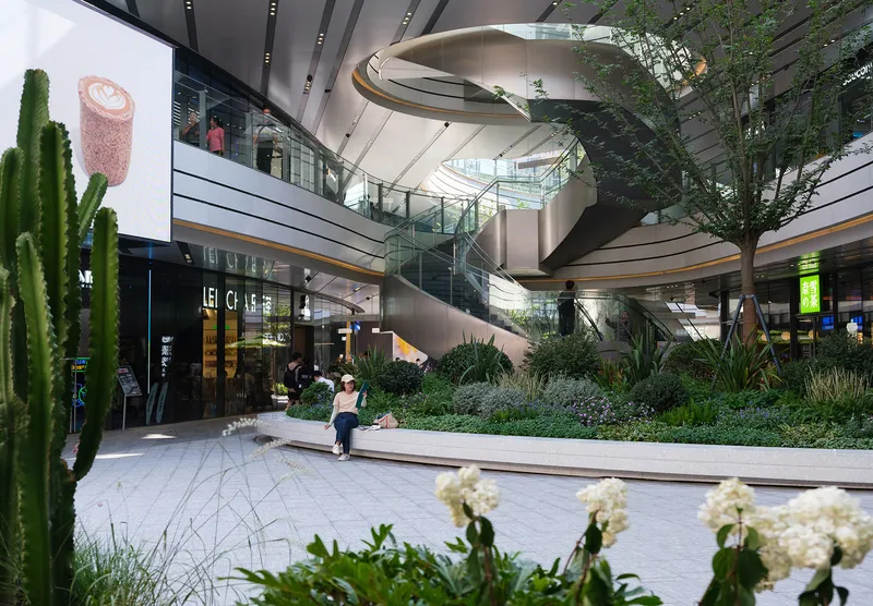 Multi-level atrium with sculptural metal staircase and planted courtyard with trees and white flowers
