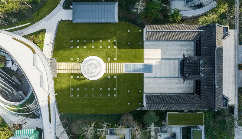 Top-down view of circular pavilion centered between traditional courtyard buildings and paved lawns