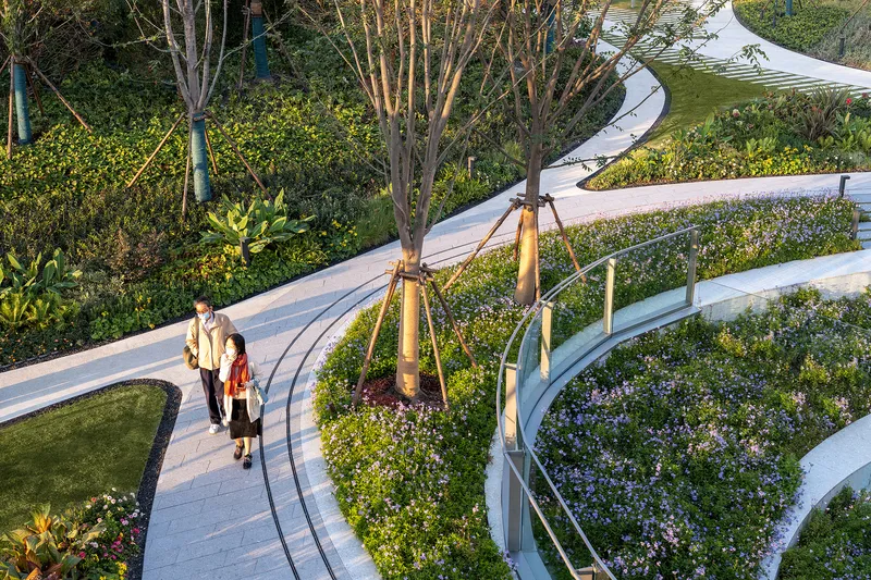Curving elevated walkway with planted beds and two people strolling in afternoon light