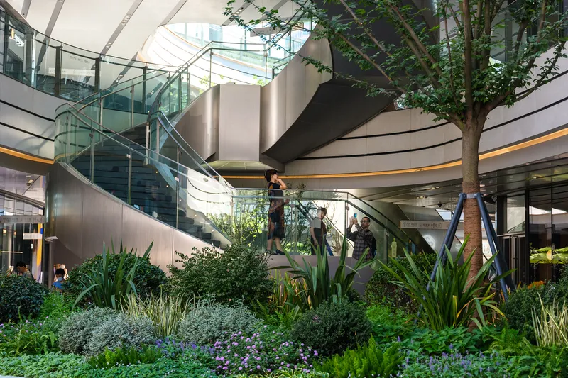 Interior atrium with planted beds surrounding sculptural steel stairs beneath a glazed skylight
