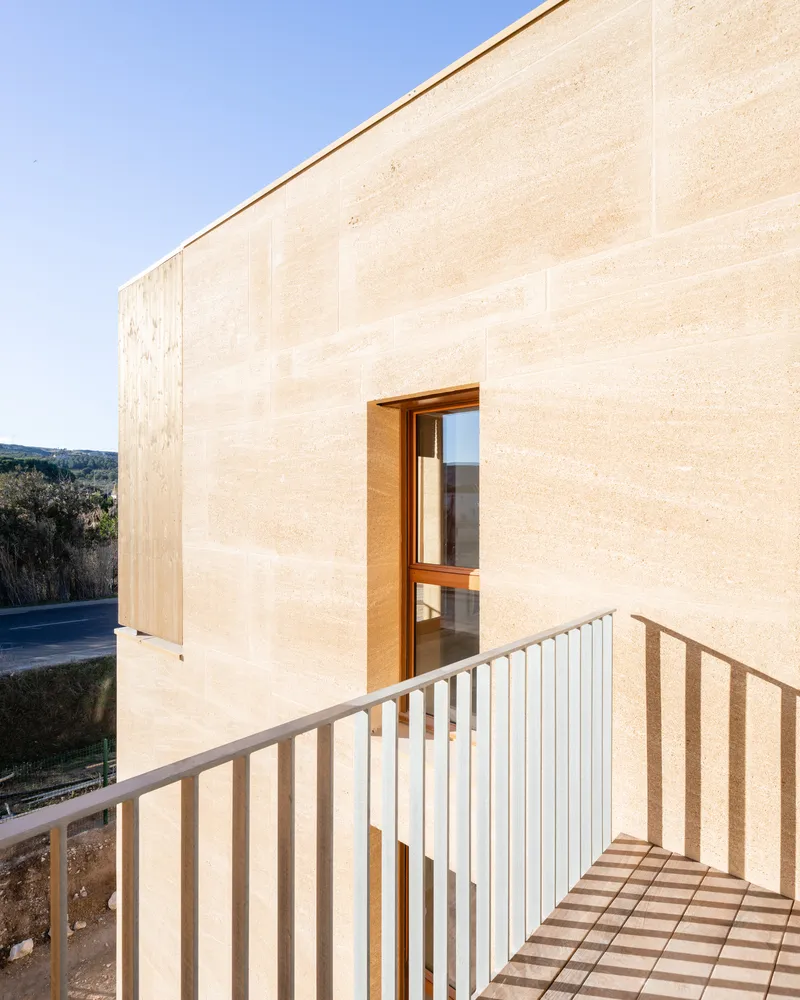 Cross-laminated timber wall with recessed doorway opening onto a pale metal railed terrace
