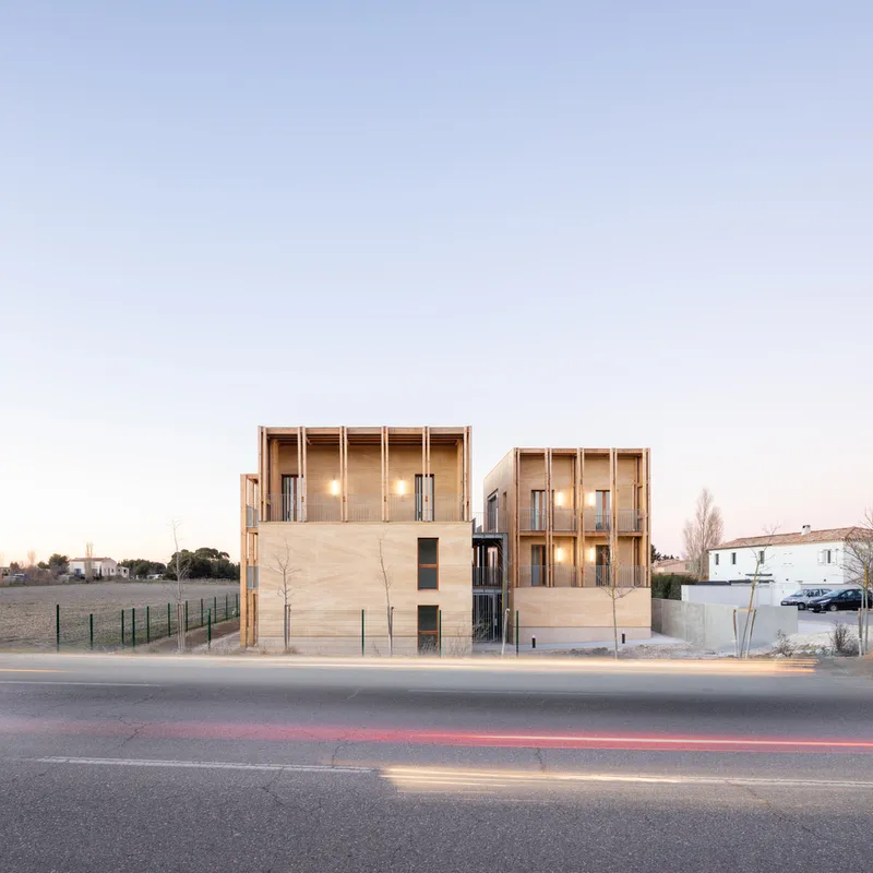 Street view of the timber-clad housing blocks with vertical window slots at dusk