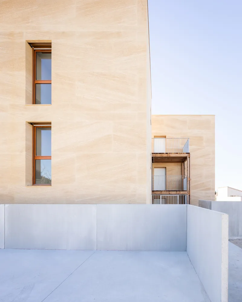 Courtyard view showing deep-set windows in the plywood facade above a white concrete plinth