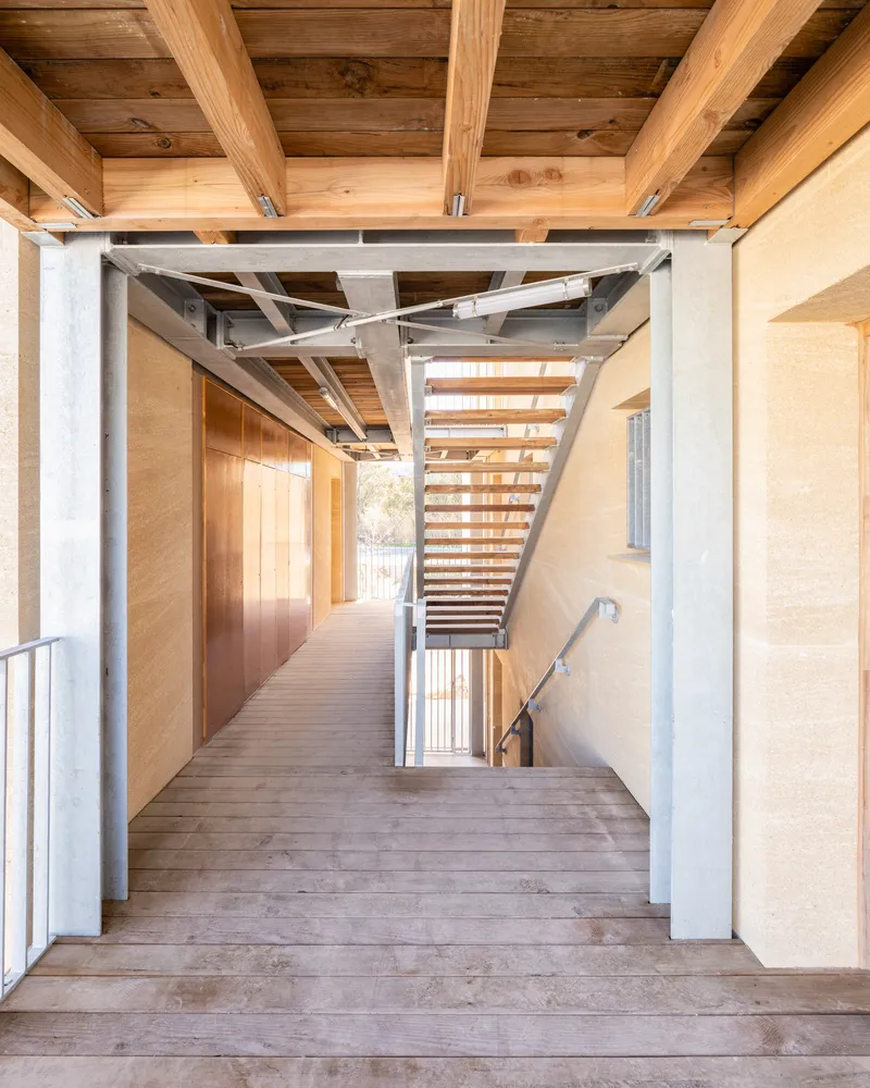 Interior corridor with exposed timber beams and steel columns leading to an open staircase
