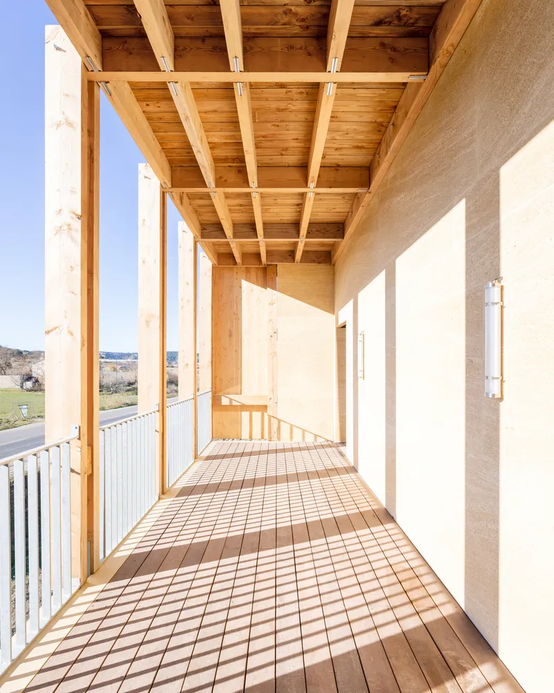 Upper-level balcony with exposed timber structure casting shadows across the slatted wood floor