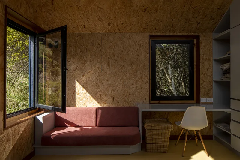 Built-in seating nook with pink cushions and oriented strand board walls framing hillside window views