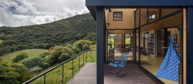 Timber deck connecting glass-walled interior to valley views with clouded sky and forested hills beyond