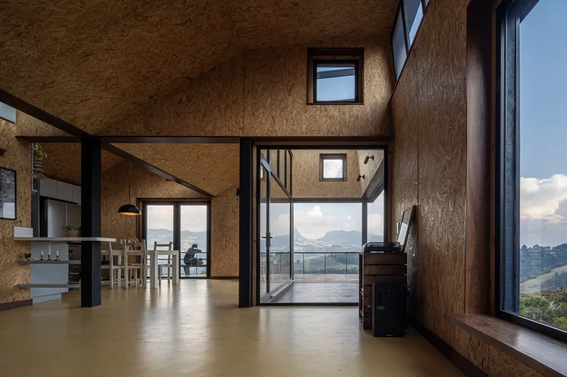Open-plan interior with oriented strand board walls and steel frame opening to glazed terrace at dusk