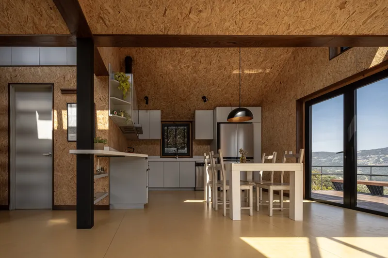 Kitchen and dining area with exposed black beams and oriented strand board ceiling lit by afternoon sun