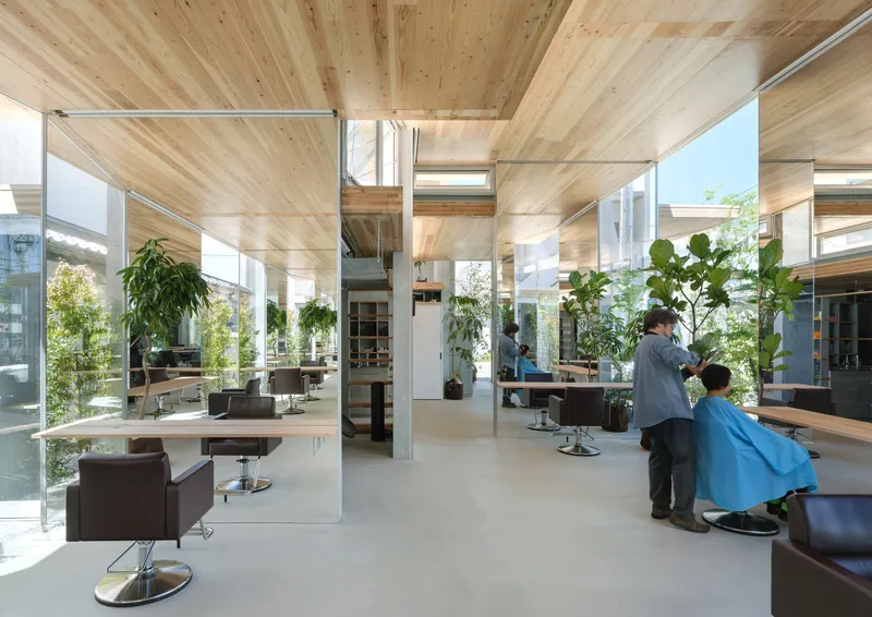 Salon interior with timber-clad ceiling, steel columns, floor-to-ceiling glass walls and potted plants throughout