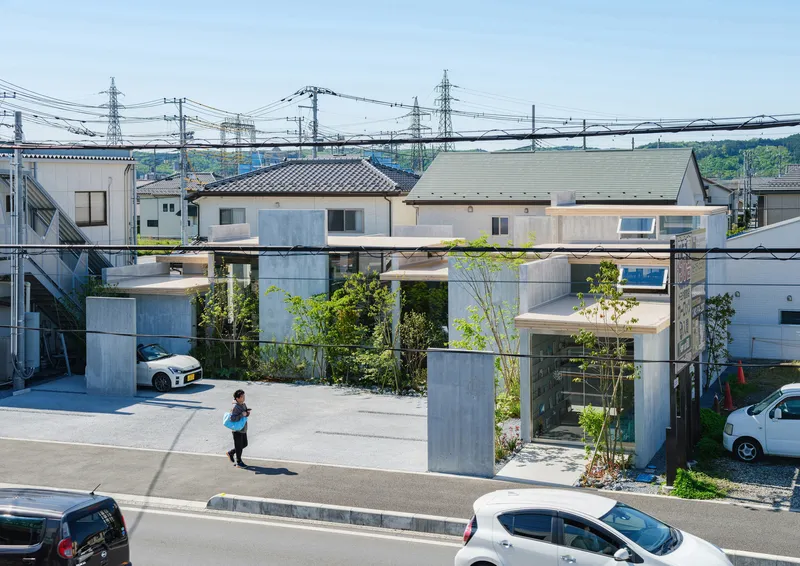 Street view of the glass-walled structure elevated on concrete columns with a child walking in the forecourt
