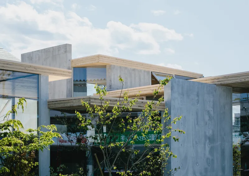 Exterior view of exposed timber beams spanning between concrete columns with young trees below