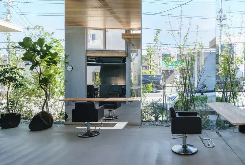Salon chair and mirrored station framed by concrete column and glass walls opening to planted edge