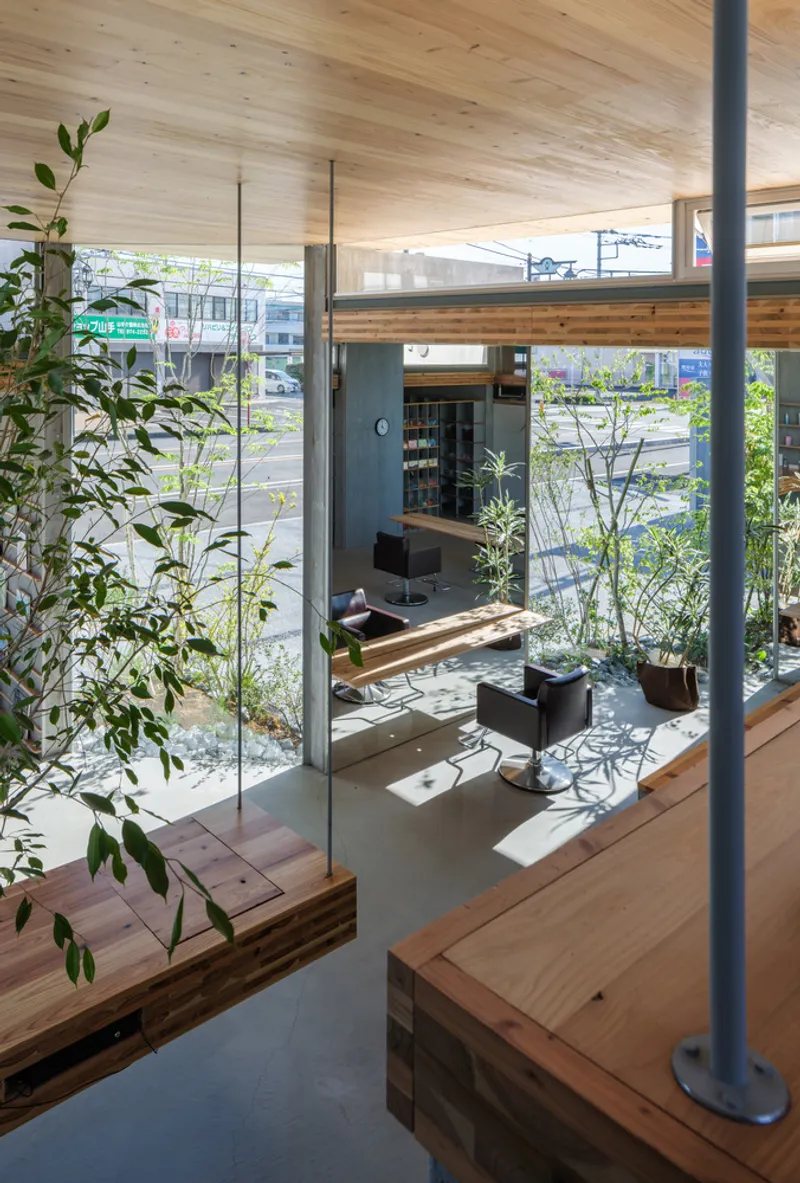Interior view through timber-framed glass partitions and planted trees into a double-height salon space below