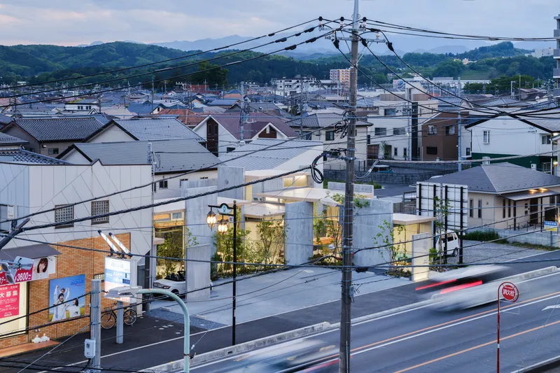 Illuminated glass facade units along a street at dusk amid a dense residential neighborhood