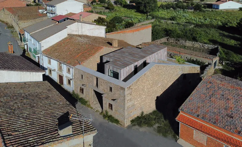 Aerial view of the timber-clad volume inserted within the cluster of tiled roofs and stone buildings