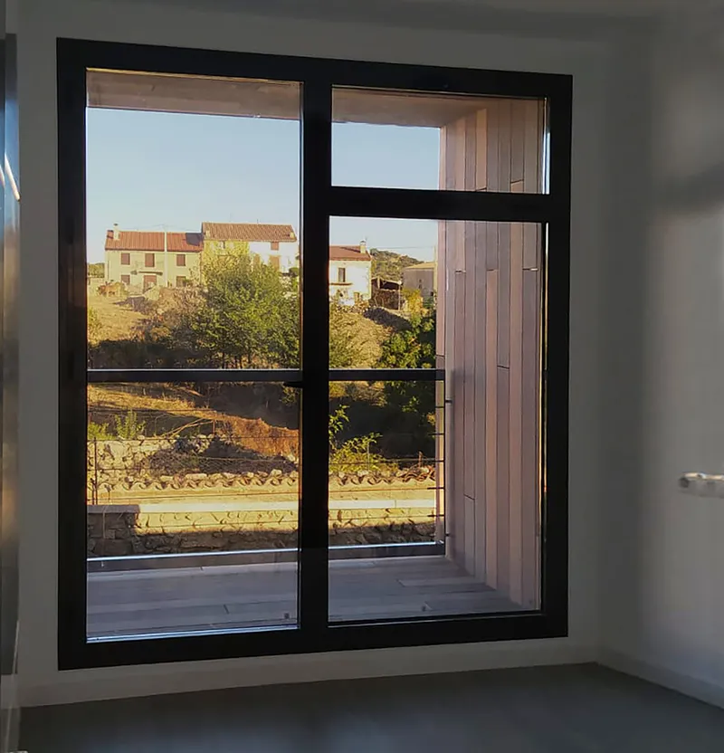 Black-framed window looking onto metal-clad facade and surrounding houses in warm afternoon light