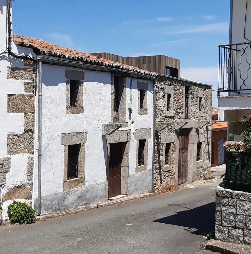 Exposed stone wall with timber lintels and a vertical timber volume visible above under clear sky