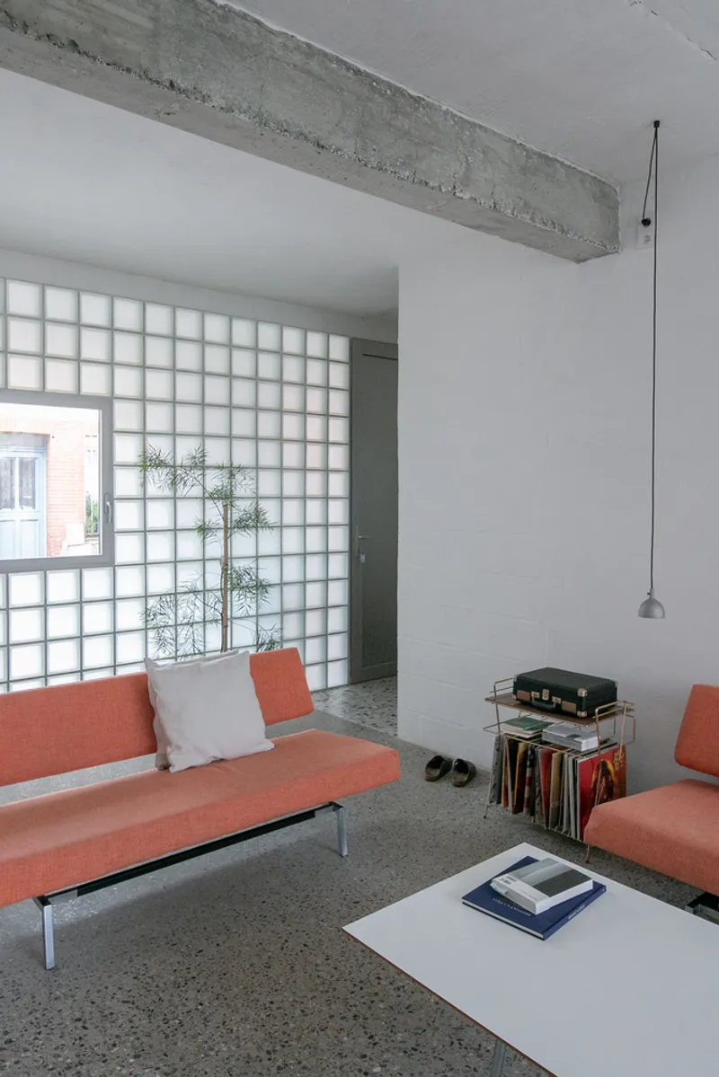 Living room with exposed concrete beam, gridded glass block wall and pendant light over terrazzo floor