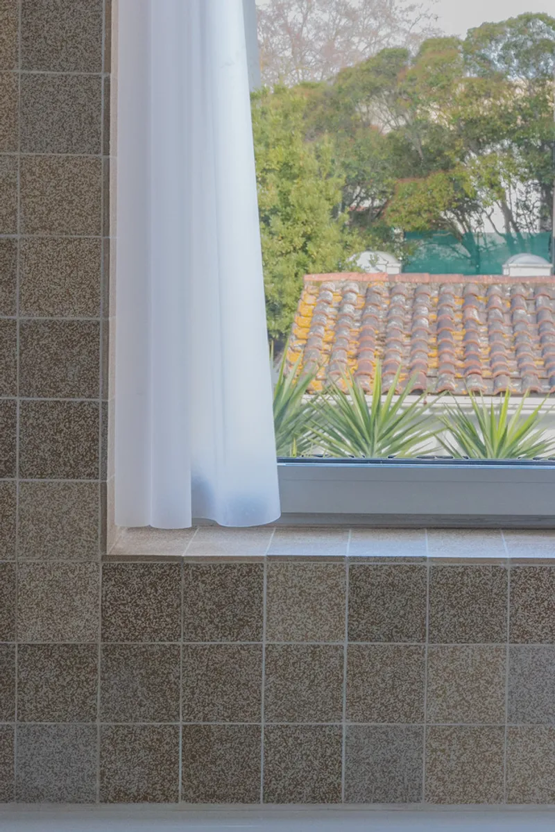 Window seat with grey terrazzo tile surround framing a view of tiled rooftops and trees