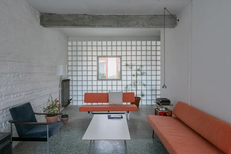 Living room with glass block wall, exposed concrete beam and terrazzo flooring with potted plants