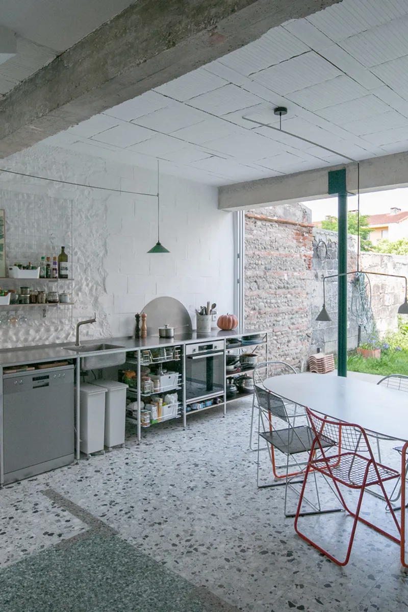 Open kitchen with suspended tile ceiling, exposed brick wall and view to garden through glazed opening