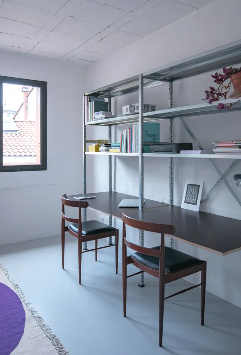 Metal shelving unit with integrated desk and two wooden chairs beneath suspended ceiling panels