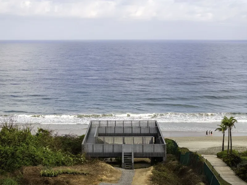 Rectangular volume clad in vertical wooden slats perched on a dune overlooking the ocean and beach