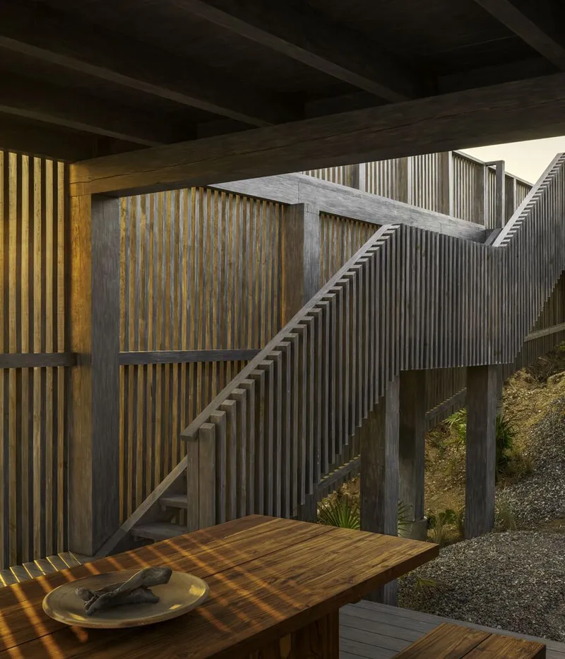 Covered terrace with exposed timber beams and slat screens casting shadows on a wooden table