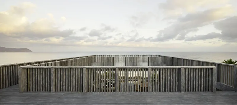Curved timber screen with vertical slats overlooking the ocean at dusk