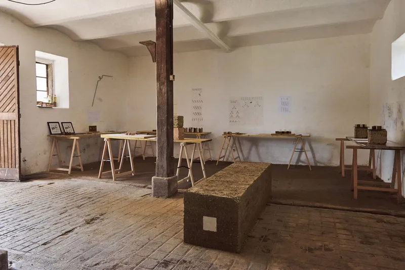 Interior workshop space with timber post, sawhorse tables, material samples and rectangular compressed earth block