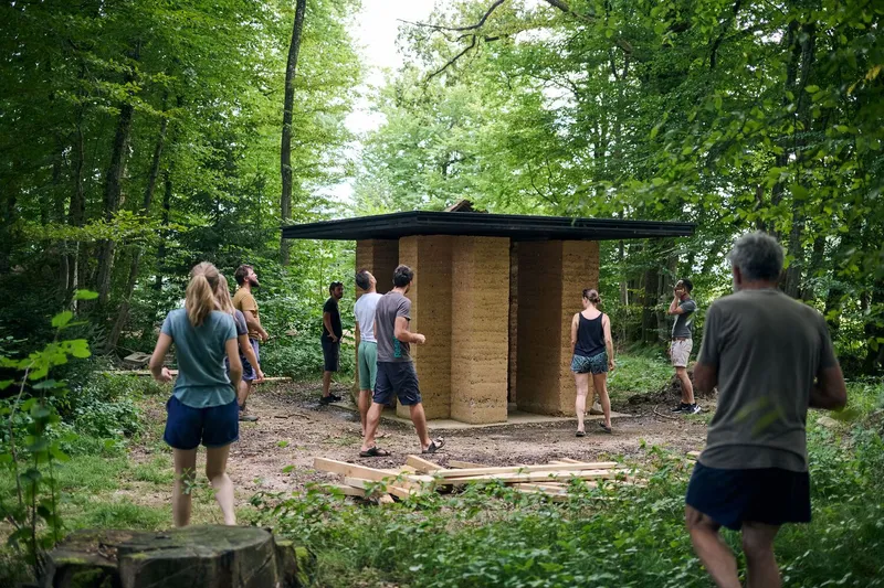 Group of visitors gathered around the rammed earth pavilion during a summer workshop in the woods