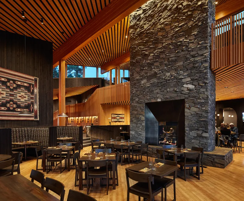 Central stone chimney with cantilevered timber ceiling planes in restaurant interior at evening