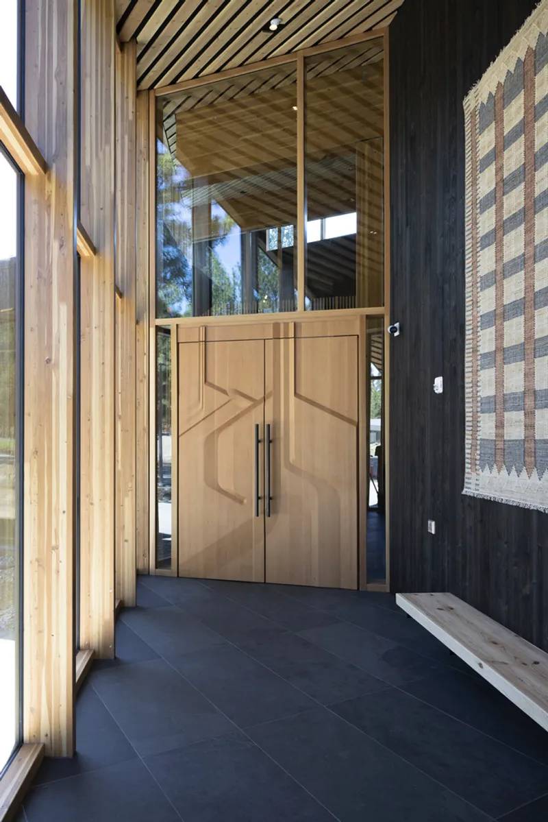 Covered entry with timber double doors, exposed wood ceiling rafters and blackened steel cladding